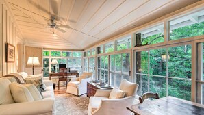 A spacious living room with a large window, a ceiling fan, and a wooden table.