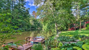 A wooden deck with a bench overlooking a pond, surrounded by lush greenery and a gazebo.