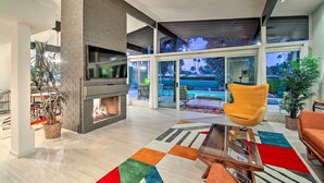 A modern living room with a fireplace, large windows, and a ceiling fan. - Palm Springs Oasis w/ Pool & Golf Course Views! (Palm Springs)