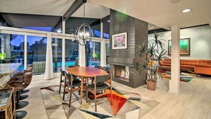 A modern dining area with a large table and chairs, a fireplace, and a view of the outdoors. - Palm Springs Oasis w/ Pool & Golf Course Views! (Palm Springs)