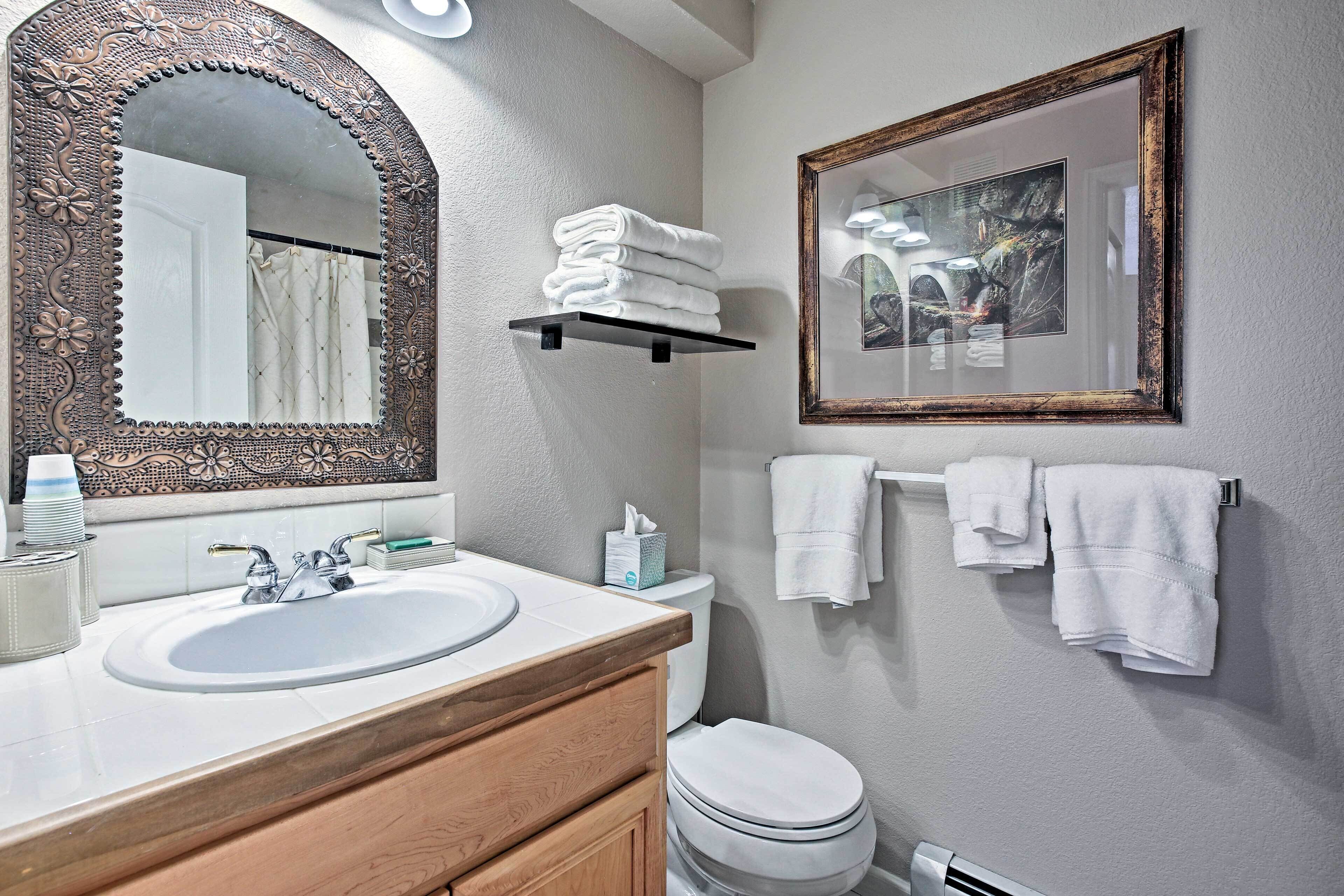 A bathroom with a large ornate mirror, a white sink, a wooden vanity, a toilet, and a framed picture on the wall.