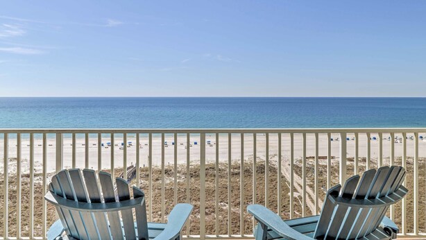A balcony with two Adirondack chairs overlooking a beach.