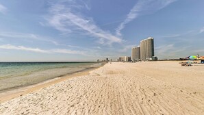 A wide sandy beach with a clear sky and a large hotel in the background.