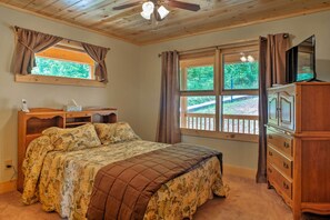 A bedroom with a bed, wooden dresser, TV, and a window with curtains.