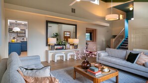 A spacious living room with a grey sofa, a coffee table with books and a vase, a staircase, and a kitchen in the background. - Family&Groups, 5br, Sleep 12, Pool/Hot tub/Firepit (Albuquerque)