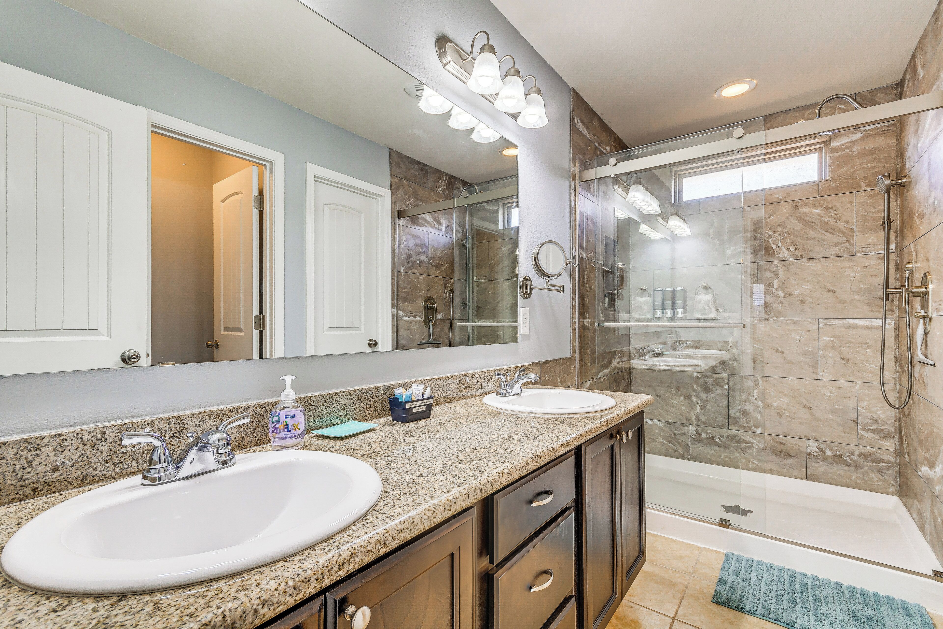 A bathroom with two sinks, a large mirror, and a glass-enclosed shower.