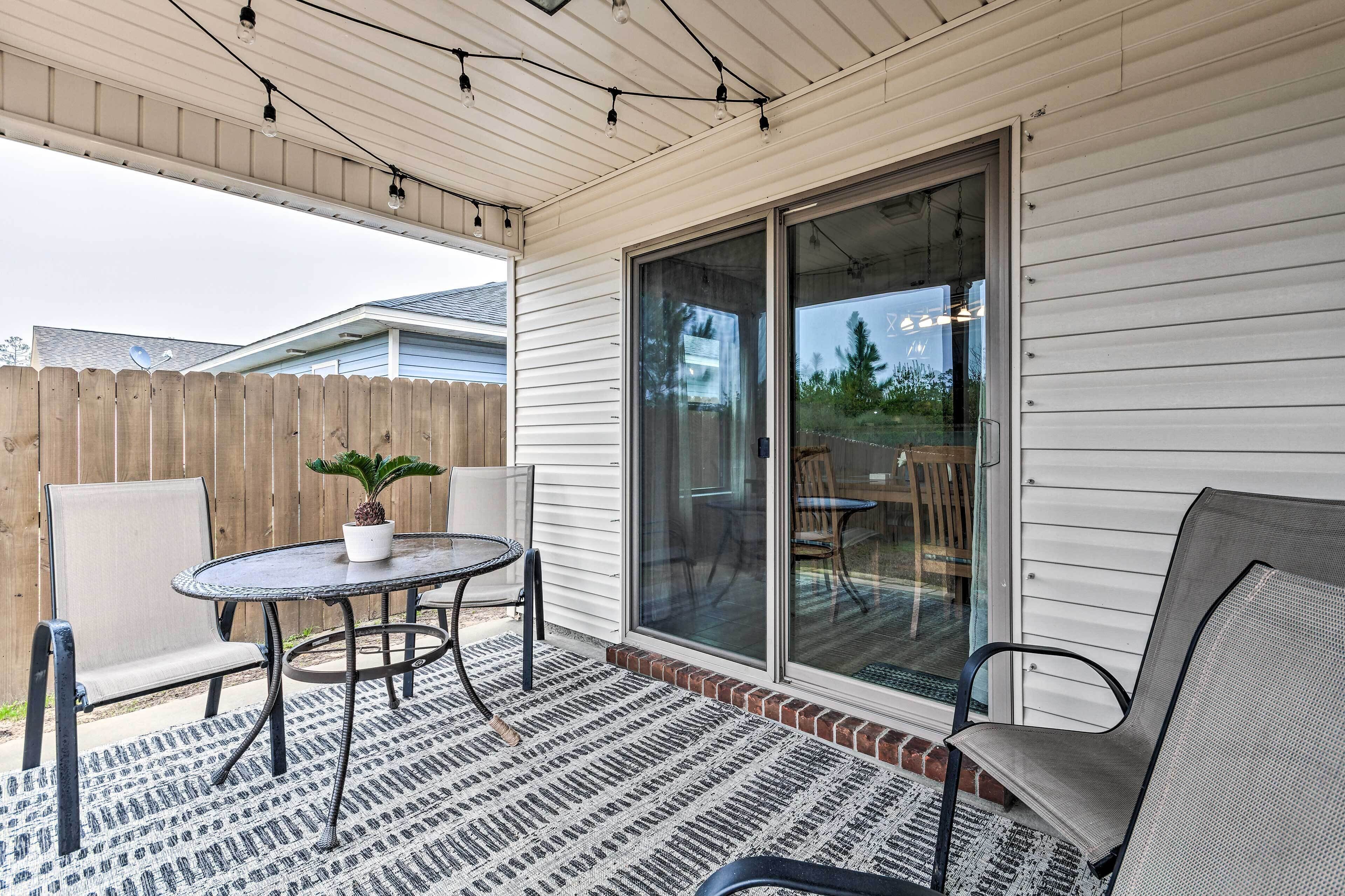 Une terrasse couverte avec une table et des chaises, une plante en pot et une porte-fenêtre coulissante donnant sur un espace extérieur.