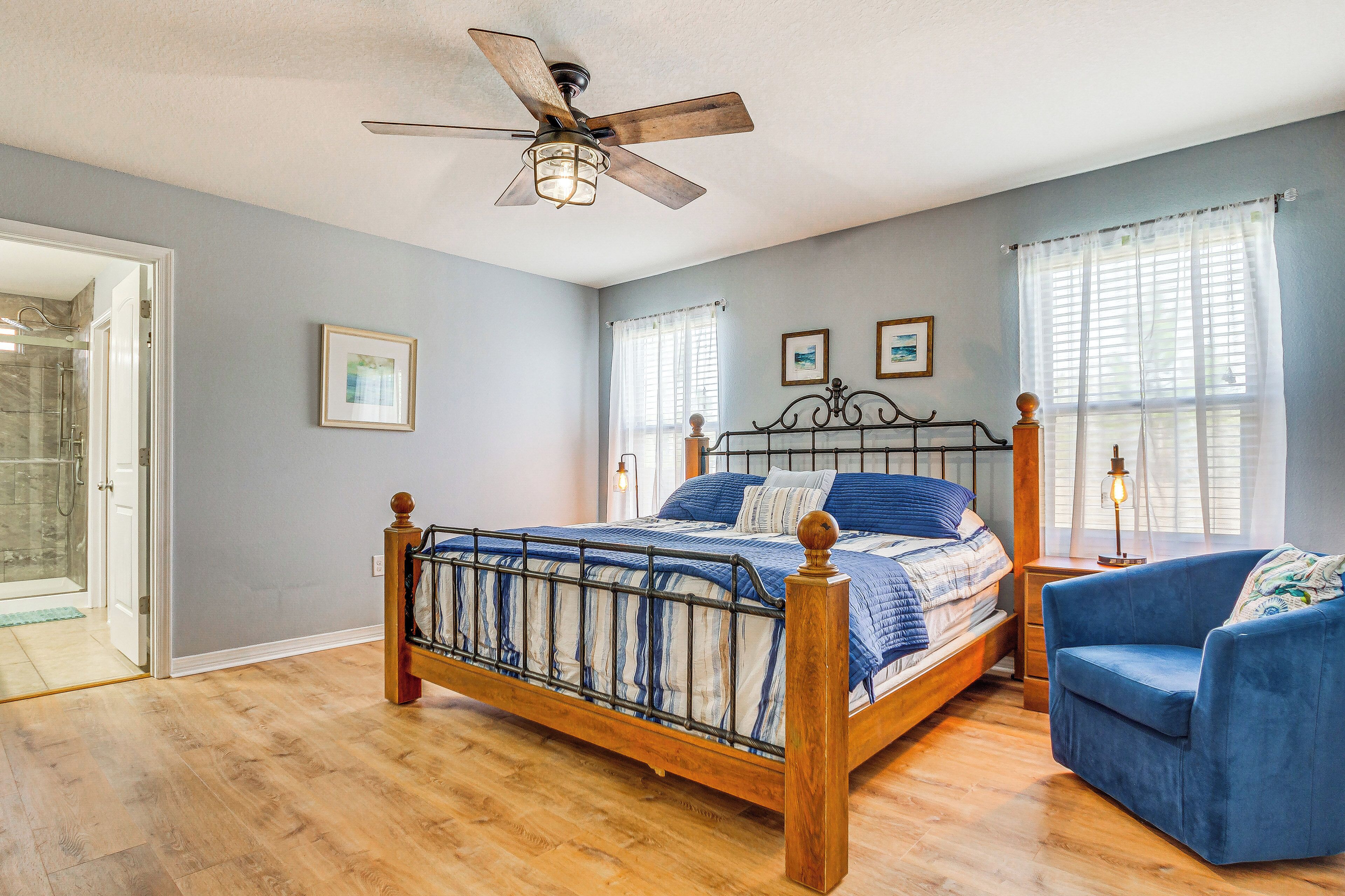 A bedroom with a wooden bed, a blue armchair, a ceiling fan, and a shower area.