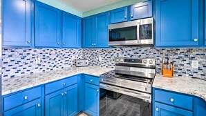 A kitchen with blue cabinets, a microwave, a stove, and a tiled backsplash. - Chic Panama City Beach Condo w/ Pool & Gulf Views (Panama City Beach)