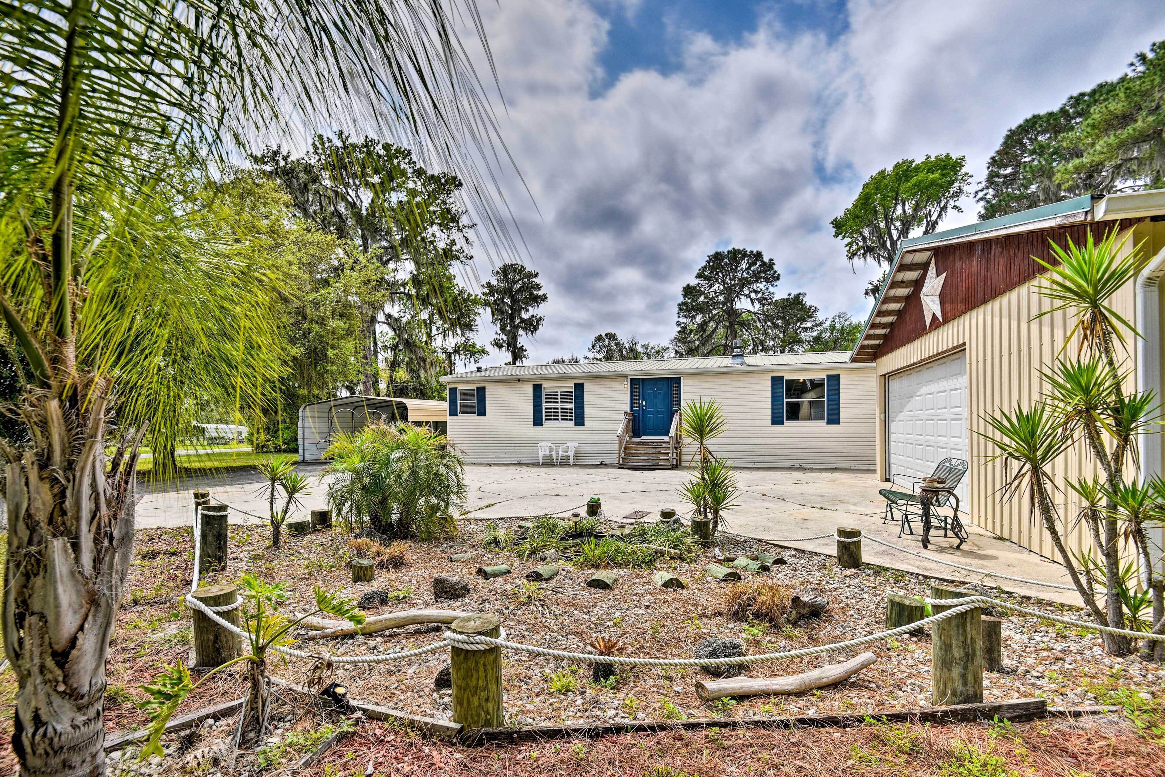 A two-story mobile home with a blue door, surrounded by a landscaped garden with various plants and a rope barrier.