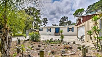 A two-story mobile home with a blue door, surrounded by a landscaped garden with various plants and a rope barrier.