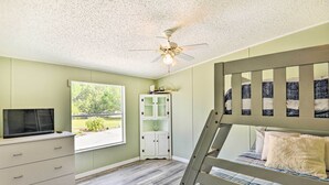 A bedroom with a bunk bed, a white dresser, a television, a ceiling fan, and a window with a view of greenery. - Waterfront Home w/ Boat Dock & Large Porch! (Georgetown)