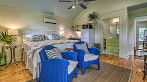 Un dormitorio con cama, dos sillas azules, ventilador de techo y kitchenette.