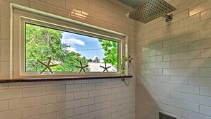 Un baño con paredes de azulejos blancos, una ventana decorada con estrellas de mar y un cabezal de ducha.