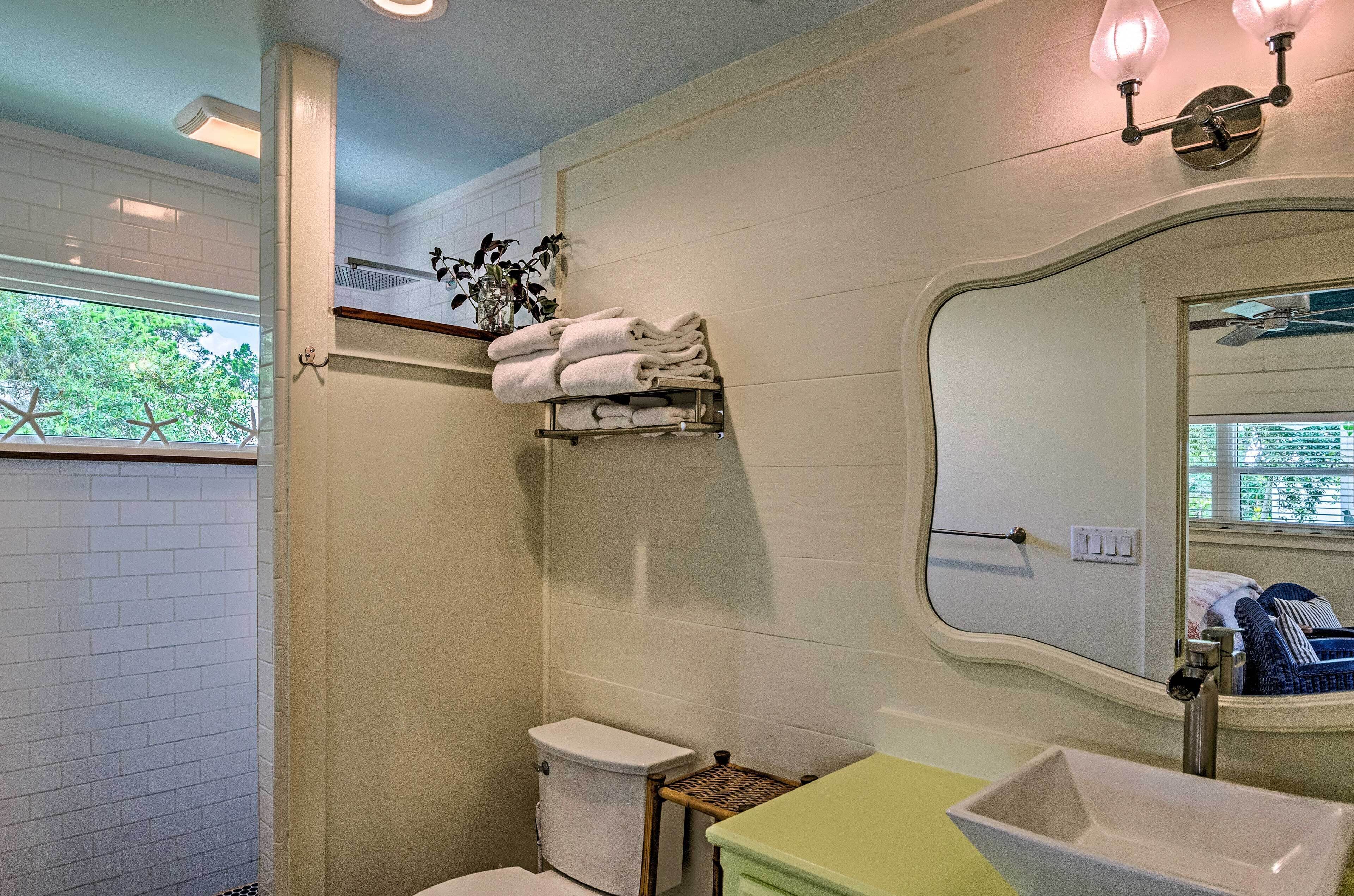 A bathroom with a toilet, sink, and shower. There is a towel rack with towels and a plant.