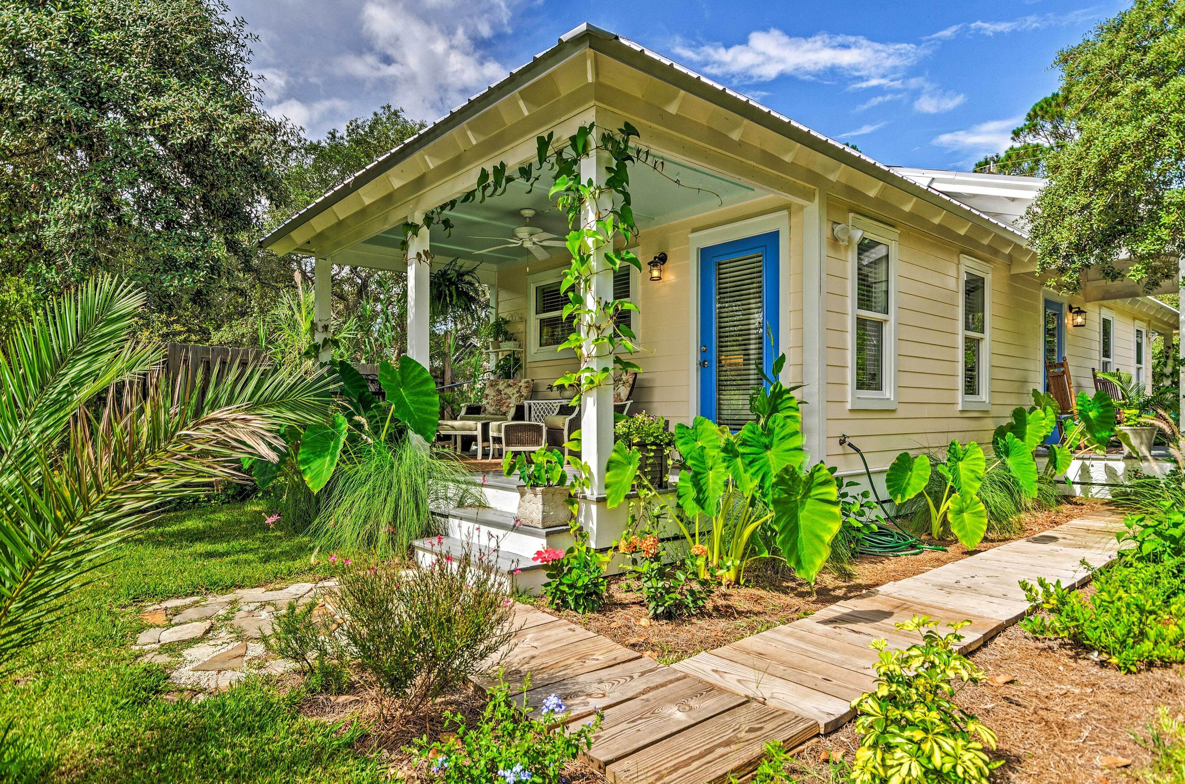 A house with a covered porch, a garden with various plants, and a wooden pathway leading to the entrance.