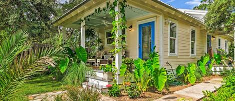 A house with a covered porch, a garden with various plants, and a wooden pathway leading to the entrance.