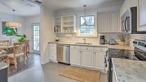 A modern kitchen with white cabinetry, stainless steel appliances, and a large window providing natural light.
