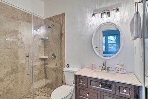 Une salle de bain avec une douche à parois de verre, des toilettes, un meuble-lavabo avec des tiroirs, un évier et un miroir avec des lumières au-dessus.