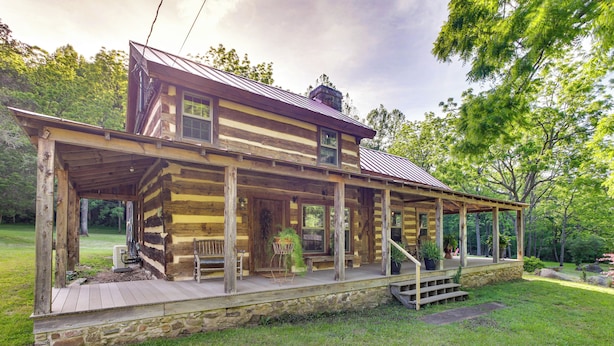 A log cabin with a porch, stone foundation, and a view of the surrounding greenery. - Restored Buchanan Log Cabin on 9-mile Creek! (Buchanan)