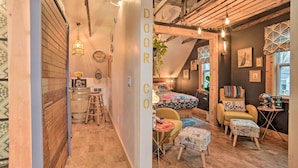 Un intérieur chaleureux avec un plancher en bois, un petit coin repas, un lit recouvert d’une couverture colorée et une chaise sur laquelle est inscrit le mot « Détente ».