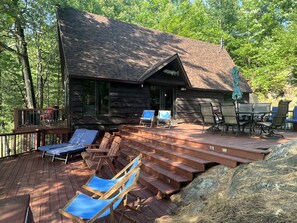 Une cabane en rondins avec une terrasse, des sièges d’extérieur et un grand rocher.