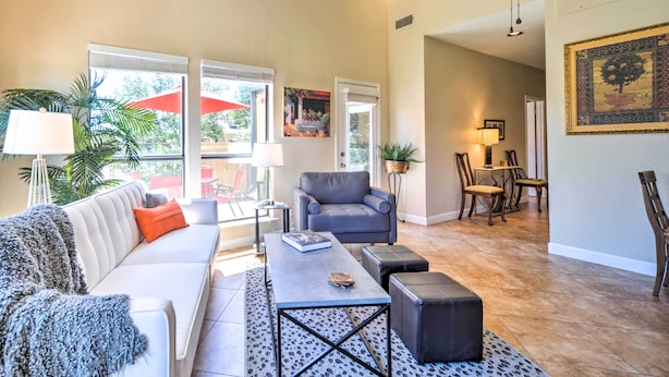 A spacious living area with a white sofa, a grey armchair, a coffee table, and a dining area with chairs and a table. - Kerrville Retreat on 18th Hole of Riverhill! (Kerrville)