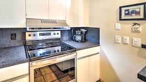 A kitchen with a stove, oven, and coffee maker. There are white cabinets and a tiled backsplash. - Kerrville Retreat on 18th Hole of Riverhill! (Kerrville)