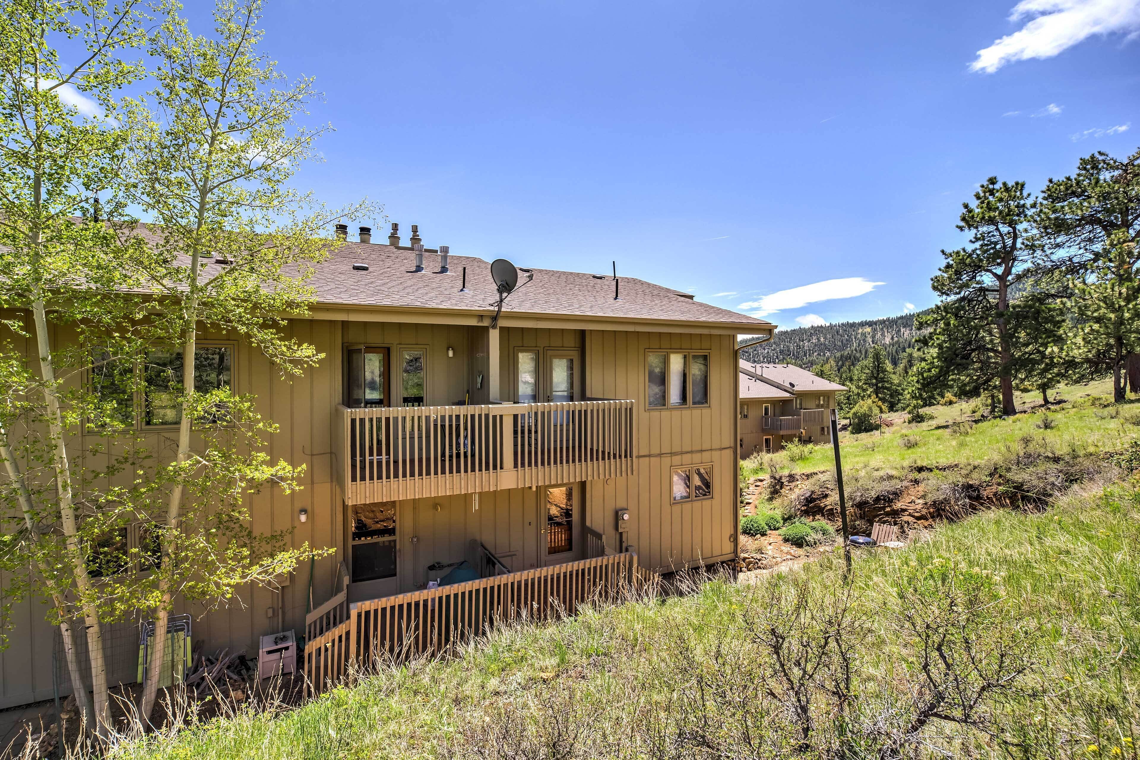 A two-story building with a balcony on the upper floor, surrounded by trees and a hilly landscape.