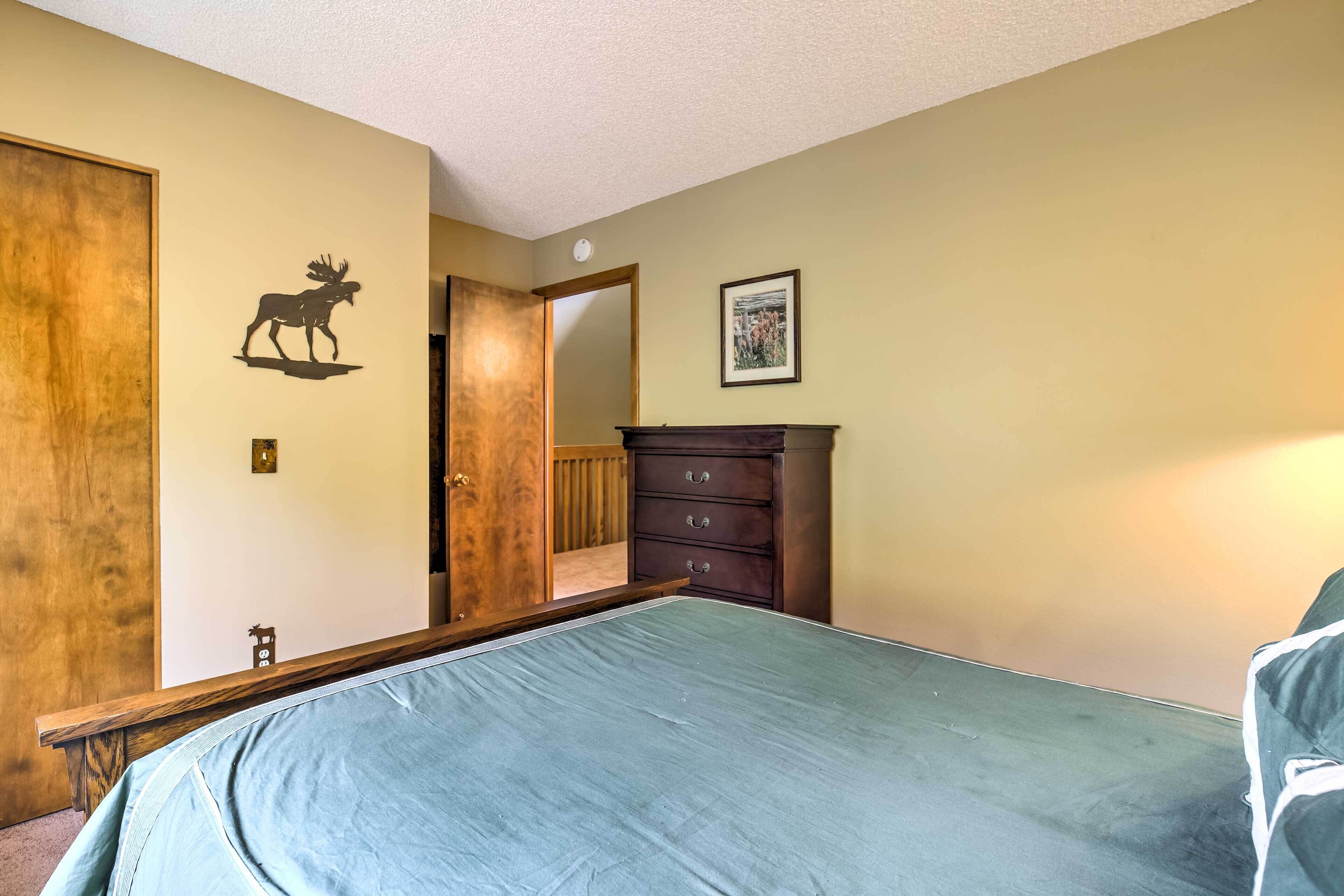 A bedroom with a bed, a dresser, a door with a moose decal, and a framed picture on the wall.