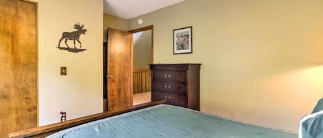 A bedroom with a bed, a dresser, a door with a moose decal, and a framed picture on the wall.