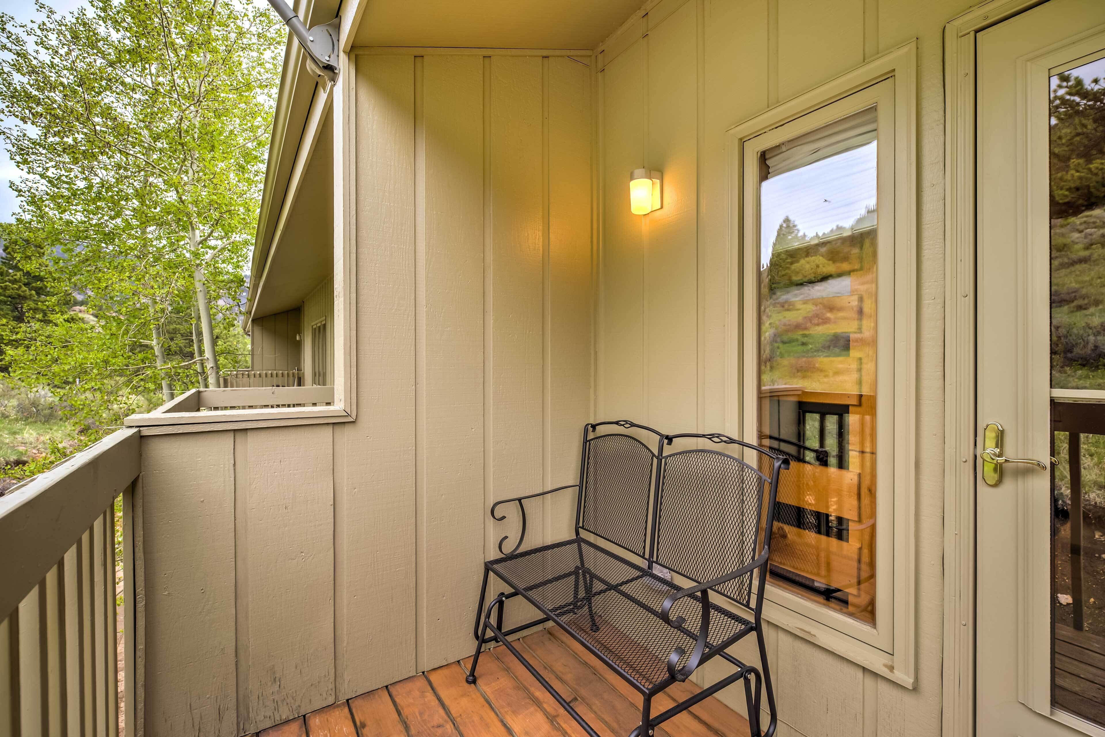 A covered porch with a metal bench, a door with a view of a landscape, and a wall-mounted light fixture.