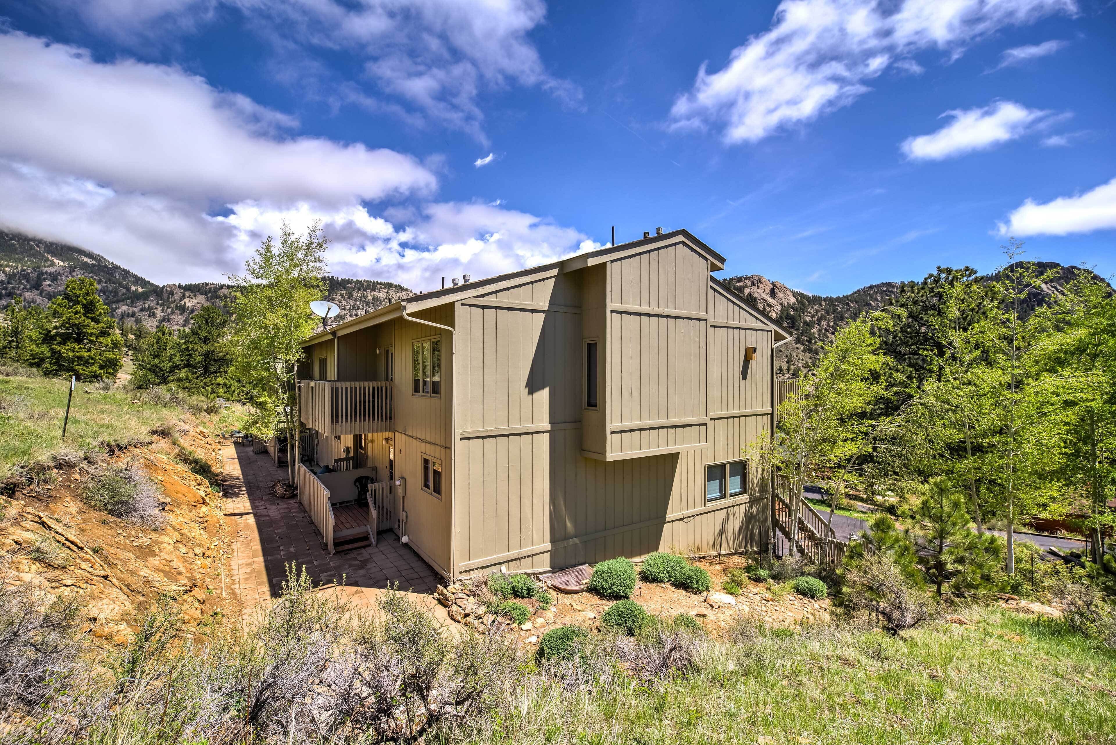 A two-story house with a deck, surrounded by a natural landscape with mountains and trees.