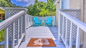 Eine Holzterrasse mit weißer Geländer, eine Fußmatte mit dem Aufdruck 'Hi!' und zwei einander zugewandte blaue Stühle.