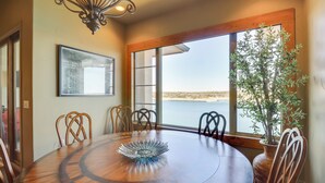 A round wooden dining table with a decorative centerpiece, surrounded by wooden chairs, in a room with large windows offering a view of the water. - Top-floor Lake-view Condo w/ Boat Dock Access (Lakeway)
