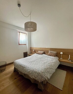 Een slaapkamer met een groot bed, een houten hoofdbord, nachtkastjes met lampen, een raam met gordijnen en een hanglamp.