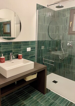 A bathroom with a sink, mirror, shower, and green-tiled walls.