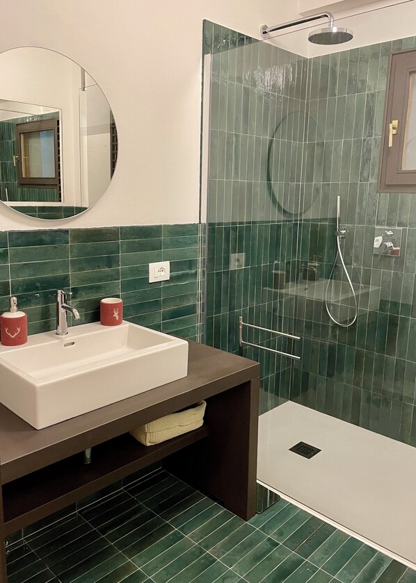 A bathroom with a sink, mirror, shower, and green-tiled walls.