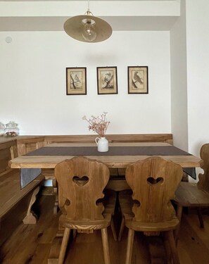 A dining area with a long wooden table, heart-shaped chairs, and three framed bird paintings on the wall.
