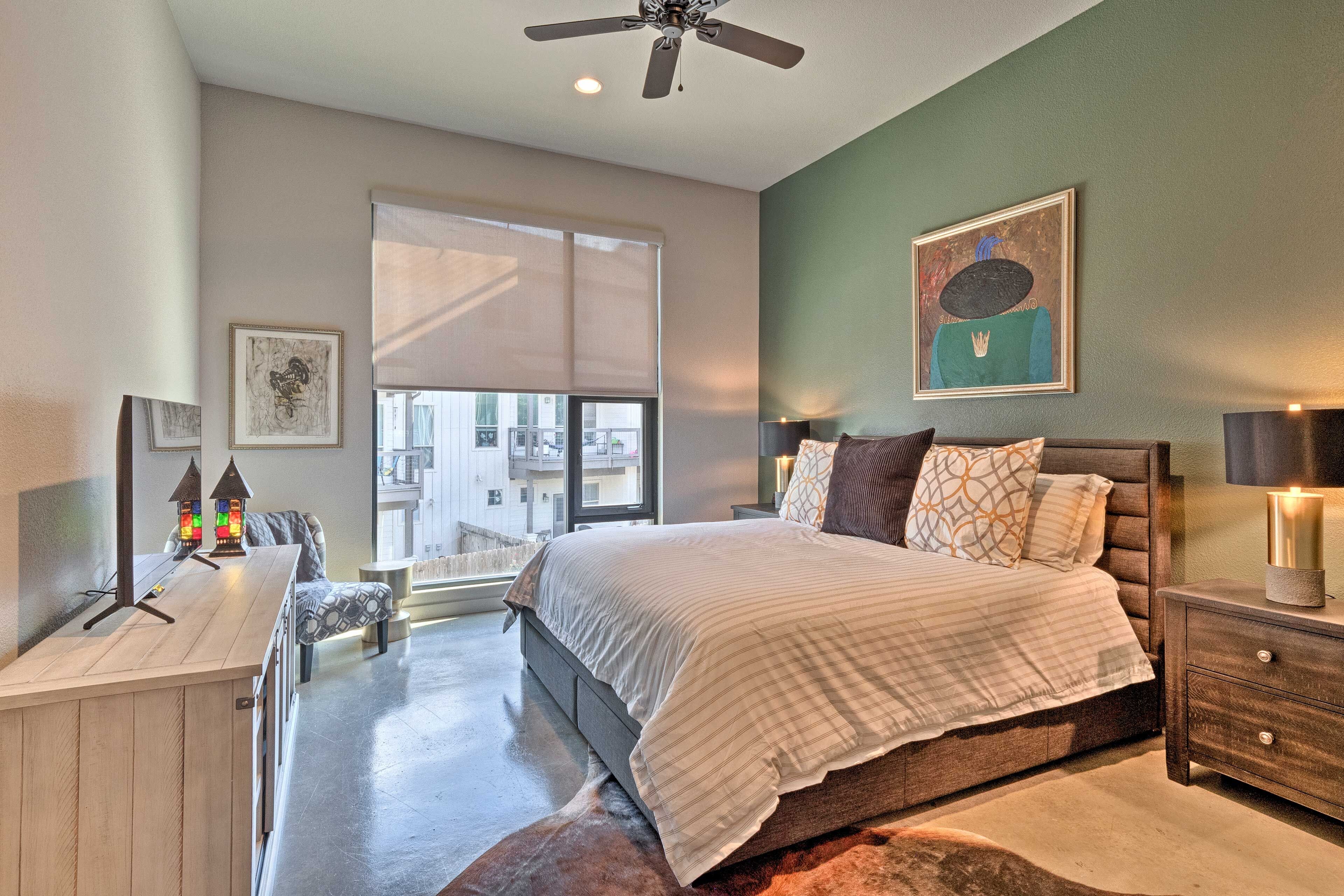 A bedroom with a large bed, a desk, a chair, a window, and a ceiling fan.