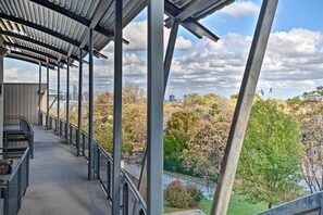 A covered outdoor area with metal railings and a concrete floor, overlooking a park with trees and a distant cityscape. - Urban Escape in Sola w/ Private Patio! (Austin)