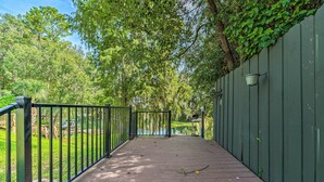 A wooden pathway with metal railings, leading to a body of water, surrounded by lush greenery and a green wall.