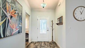 A hallway with a wooden floor, a white door with a glass window, a wall clock, and a framed picture.