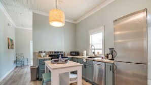 Una cocina moderna con un refrigerador de acero inoxidable, un microondas y un lavamanos. Hay una mesa de comedor de madera con sillas y una lámpara colgante.
