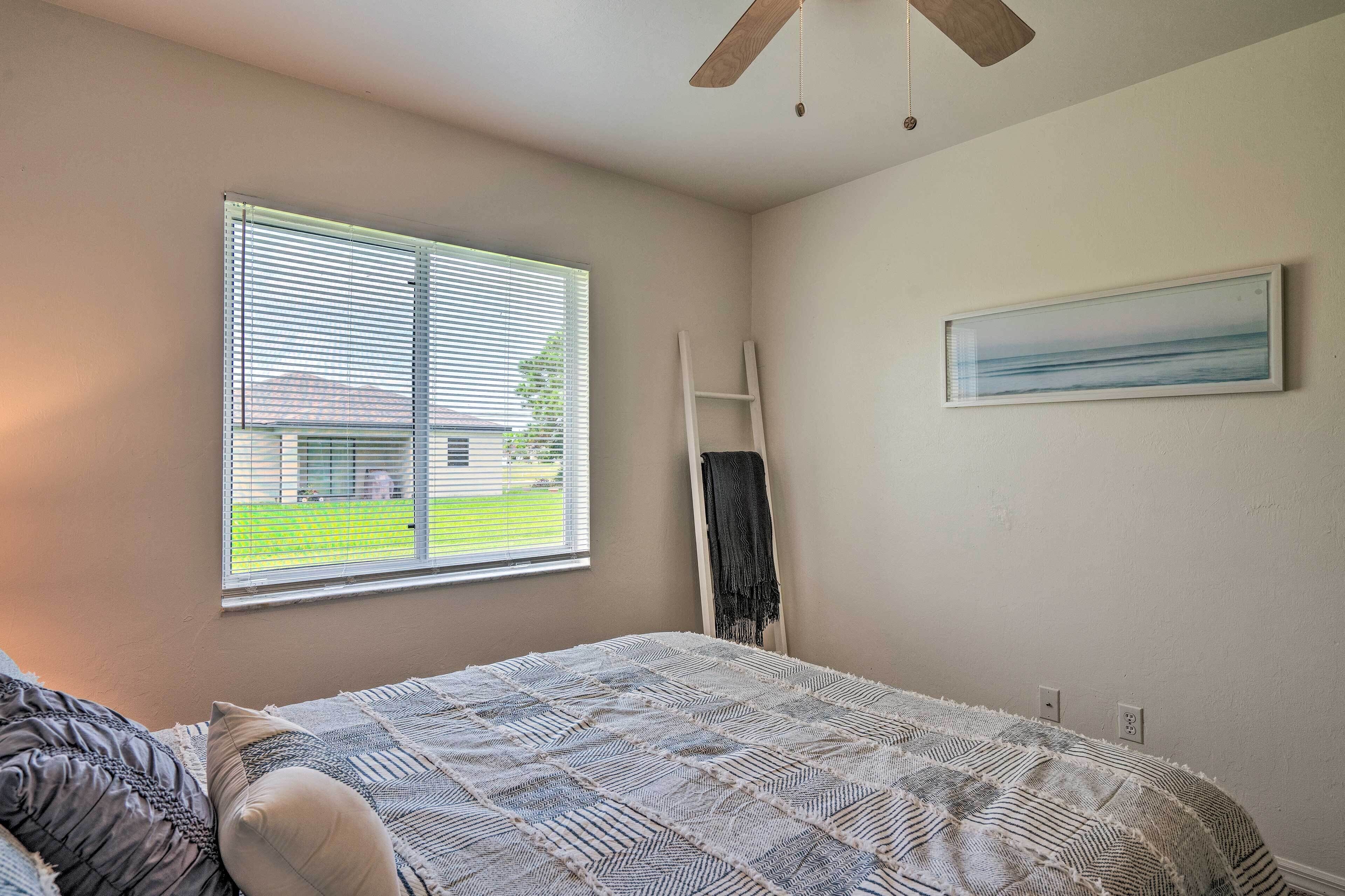 A bedroom with a bed, a window with blinds, a ladder, and a painting on the wall.