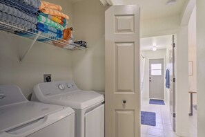 Un lavadero con un tendedero apilado, lavadora y secadora, y una puerta que da a otra habitación.