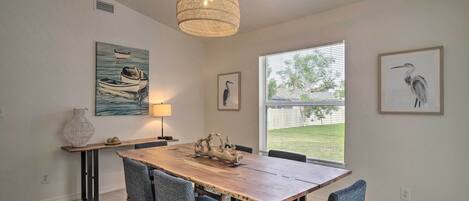 Un comedor con una mesa de madera, cuatro sillas, una lámpara colgante y obras de arte en las paredes.