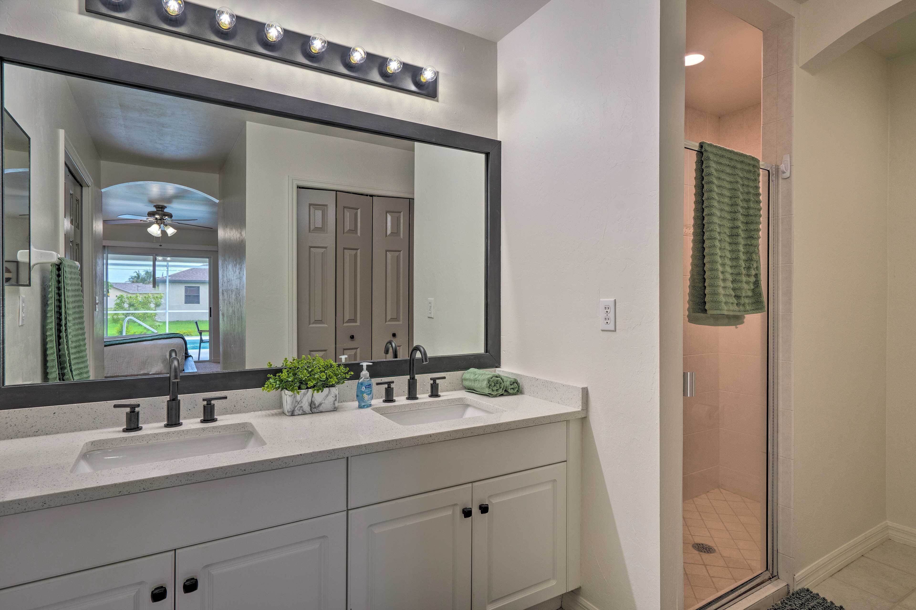 A bathroom with a large mirror, two sinks, a shower, and a ceiling fan.