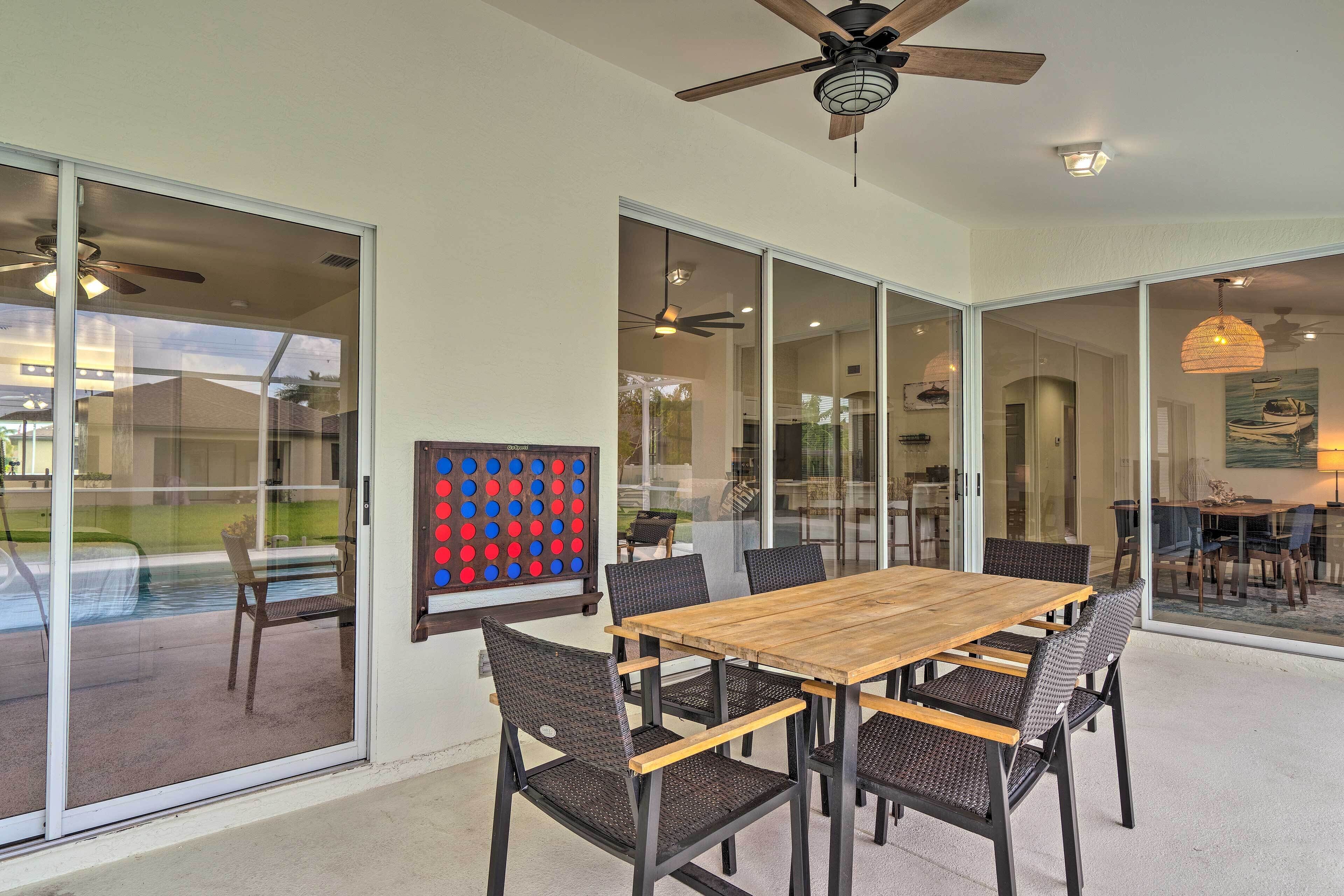 A spacious dining area with a wooden table and wicker chairs, large glass sliding doors, ceiling fans, and a view of the outdoors.