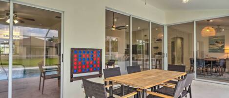 A spacious dining area with a wooden table and wicker chairs, large glass sliding doors, ceiling fans, and a view of the outdoors.